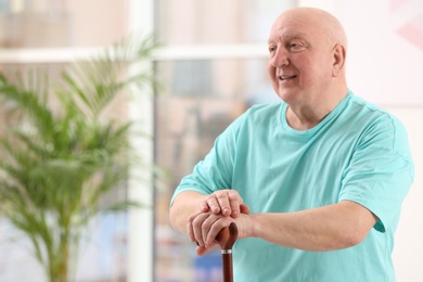 Photo of Elderly man with cane in nursing home, space for text. Assisting senior generation