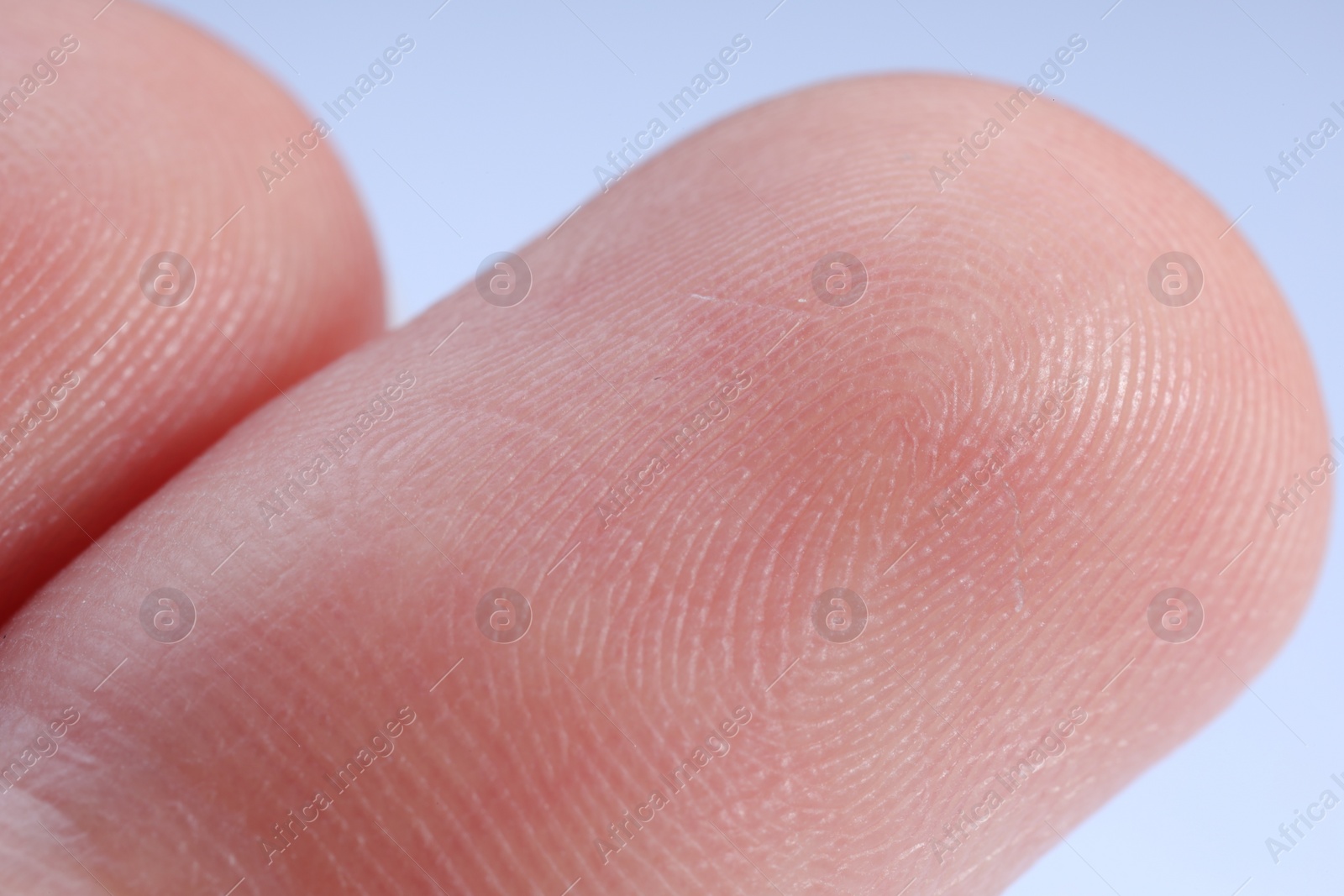 Photo of Finger with friction ridges on light blue background, macro view