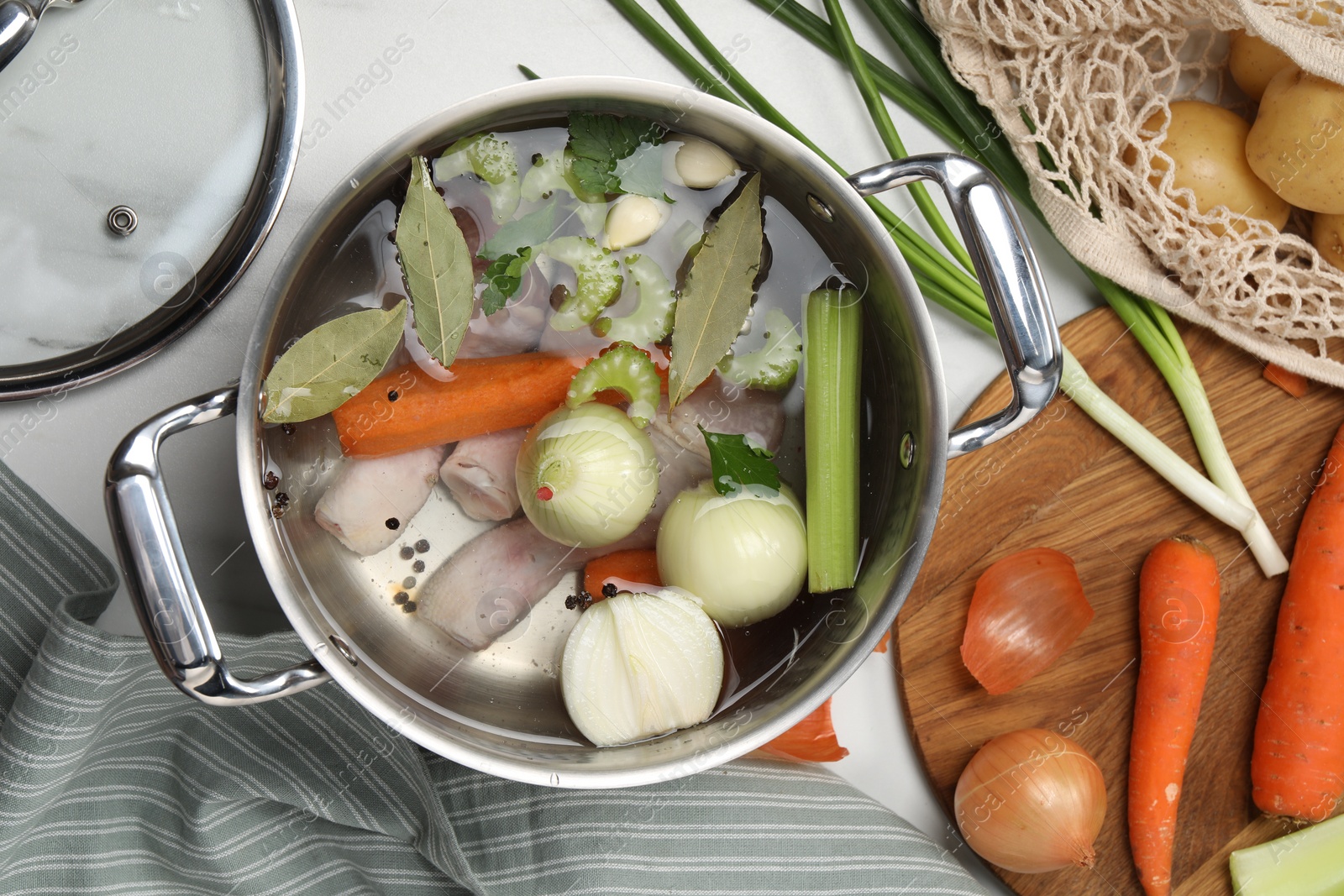 Photo of Pot and different ingredients for cooking tasty bouillon on white marble table, flat lay