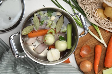 Pot and different ingredients for cooking tasty bouillon on white marble table, flat lay