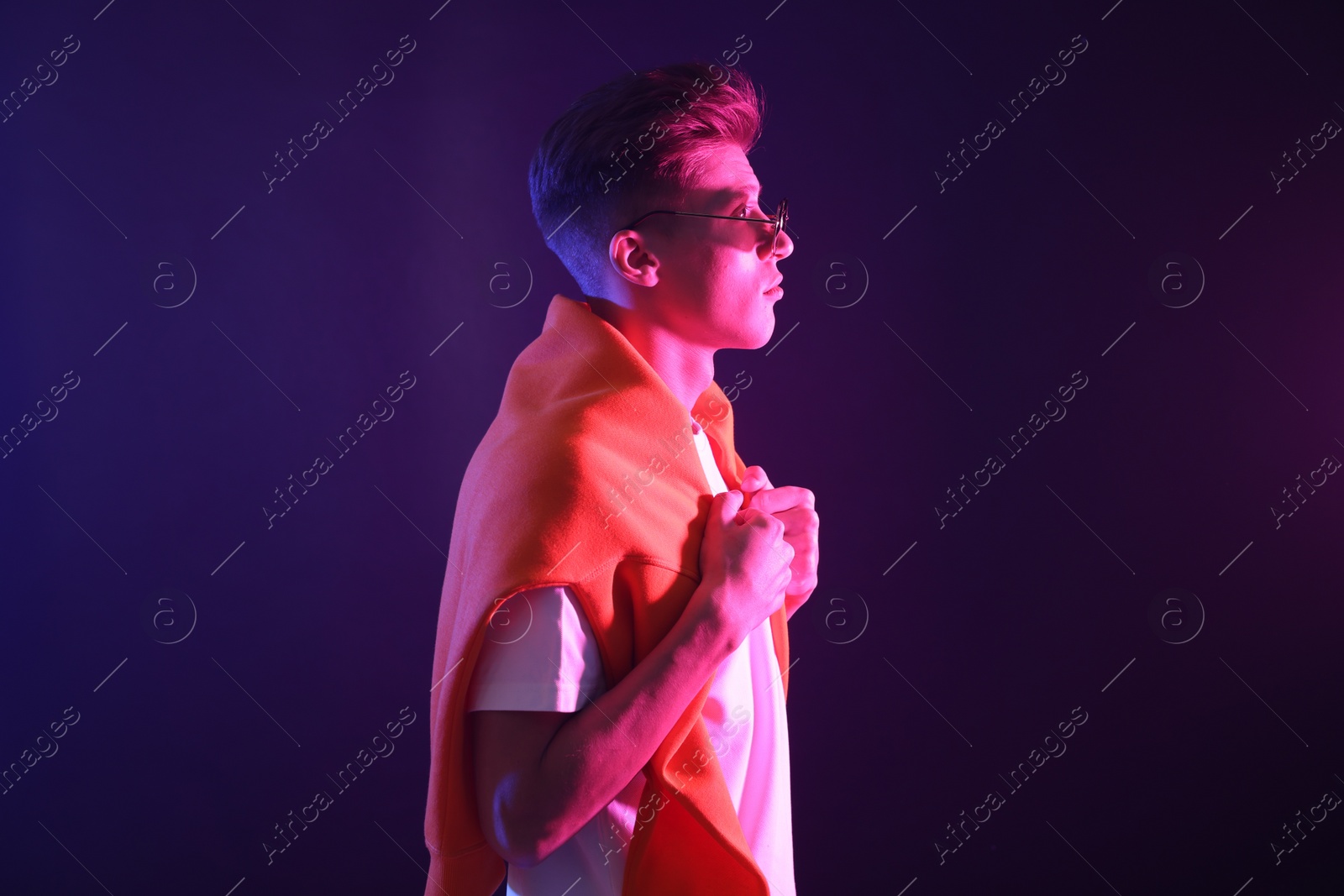 Photo of Stylish young man in sunglasses on dark background in neon lights