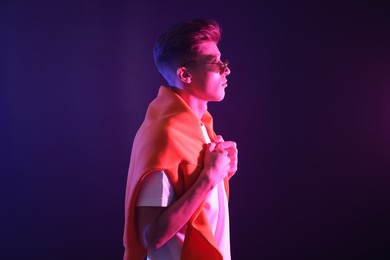 Stylish young man in sunglasses on dark background in neon lights