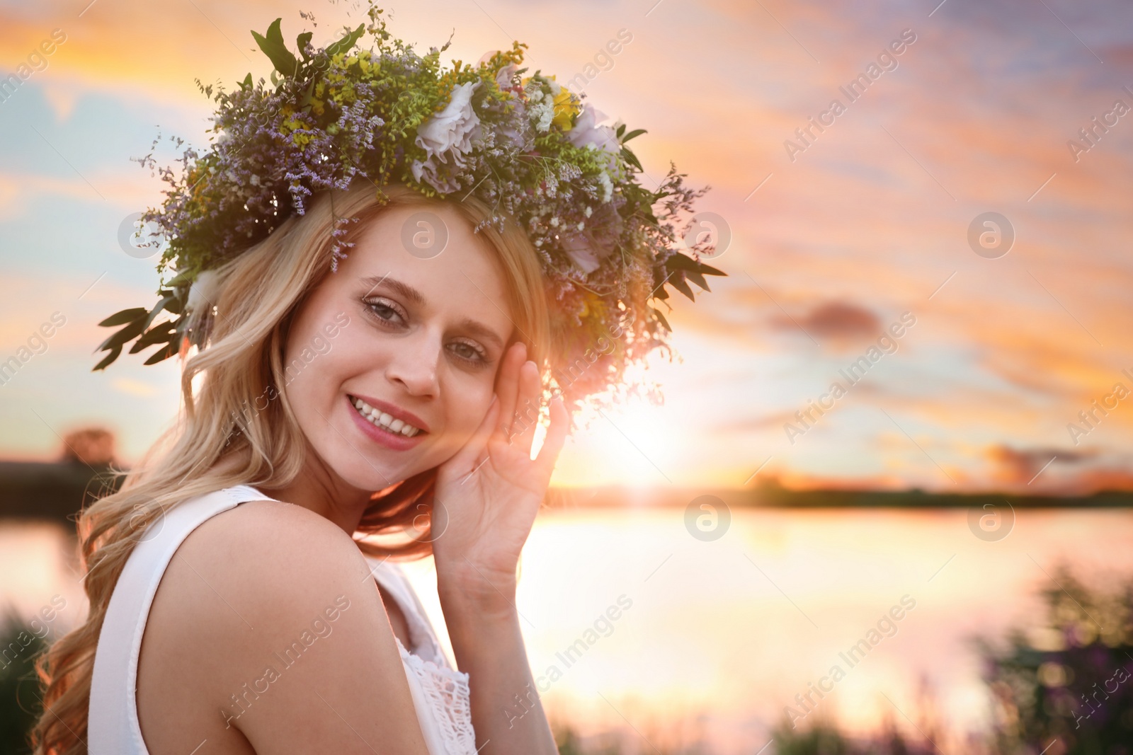 Photo of Young woman wearing wreath made of beautiful flowers outdoors at sunset