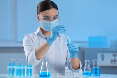 Scientist taking sample of light blue liquid and glassware in laboratory
