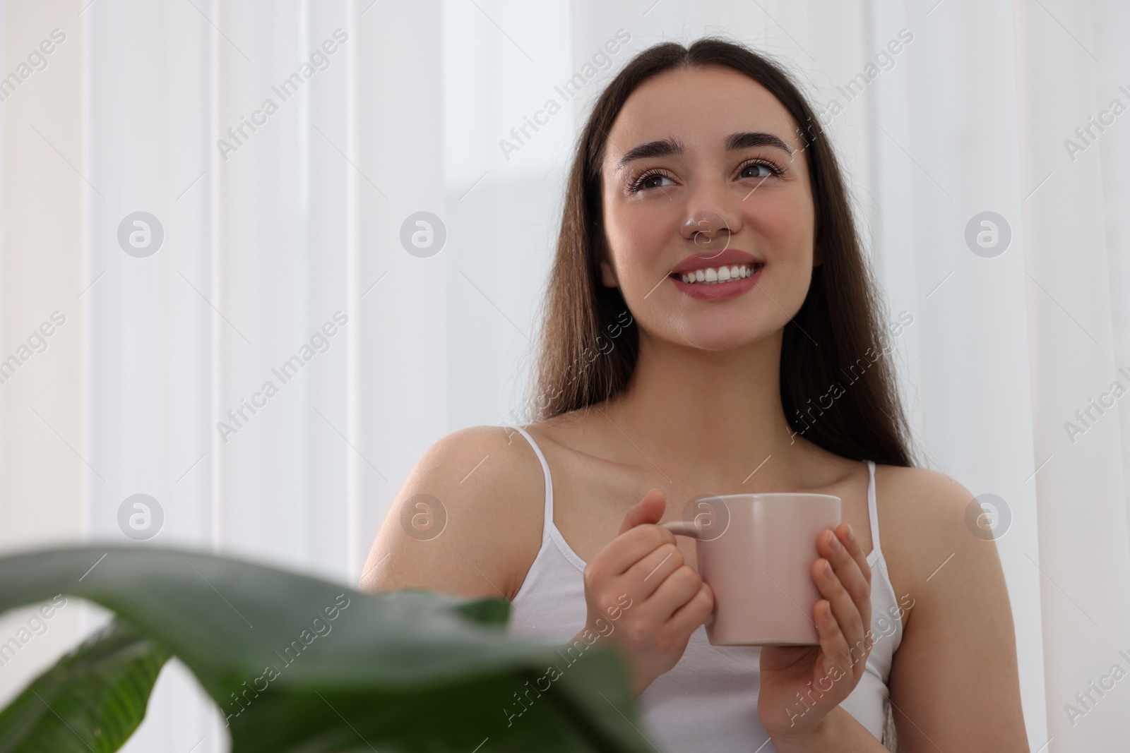 Photo of Happy woman with cup of drink near window indoors, space for text. Lazy morning