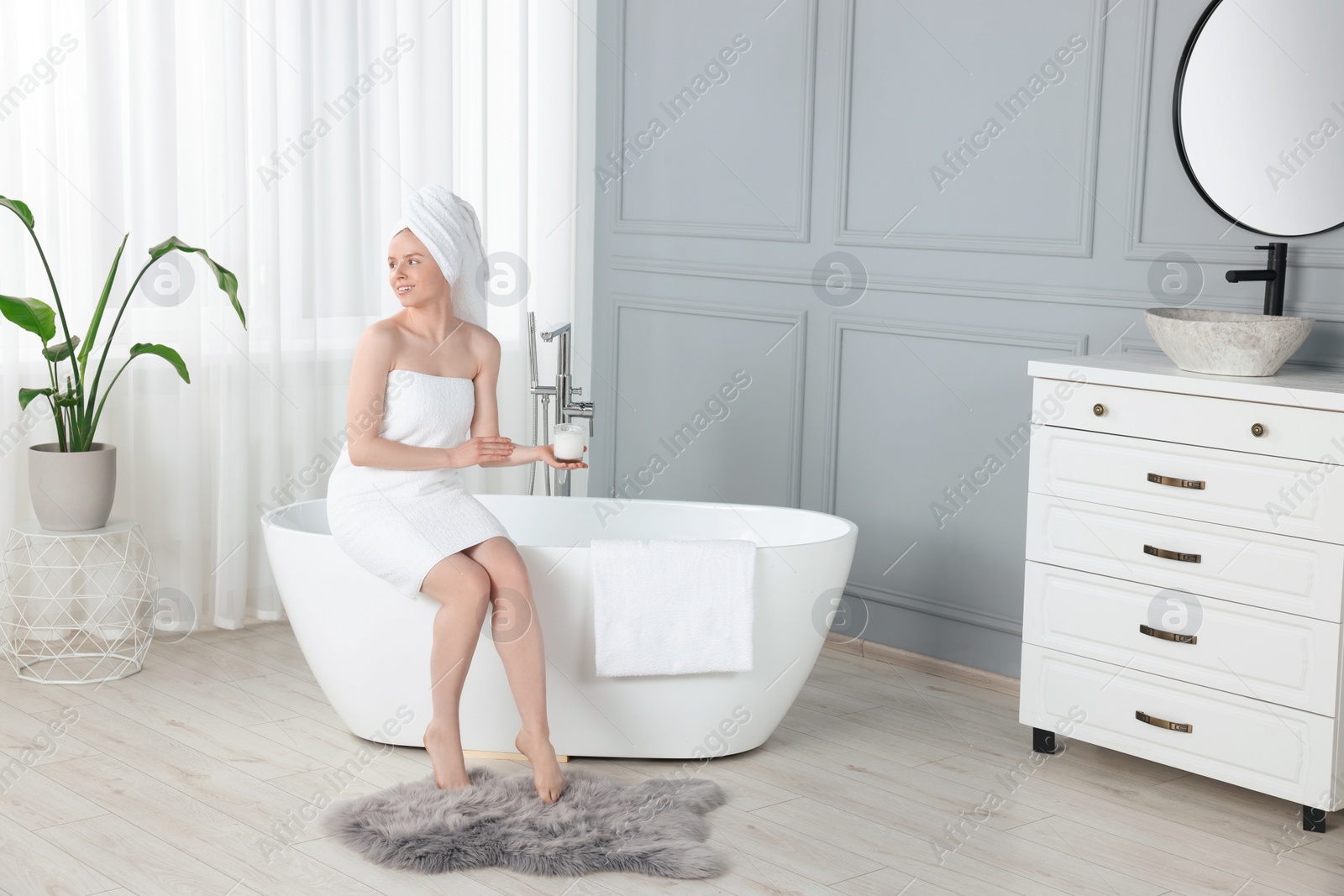 Photo of Beautiful young woman applying body cream onto arm in bathroom