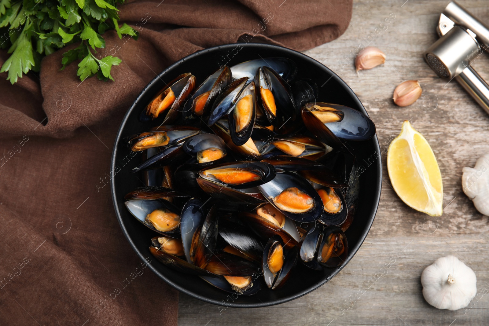 Photo of Bowl of delicious cooked mussels with parsley, garlic and lemon on wooden table, flat lay