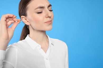 Photo of Young woman cleaning ear with cotton swab on light blue background, closeup. Space for text