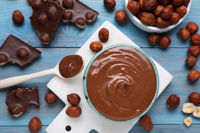 Photo of Bowl with tasty paste, chocolate pieces and nuts on light blue wooden table, flat lay