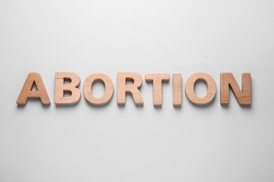 Photo of Word Abortion made of wooden letters on light grey background, flat lay