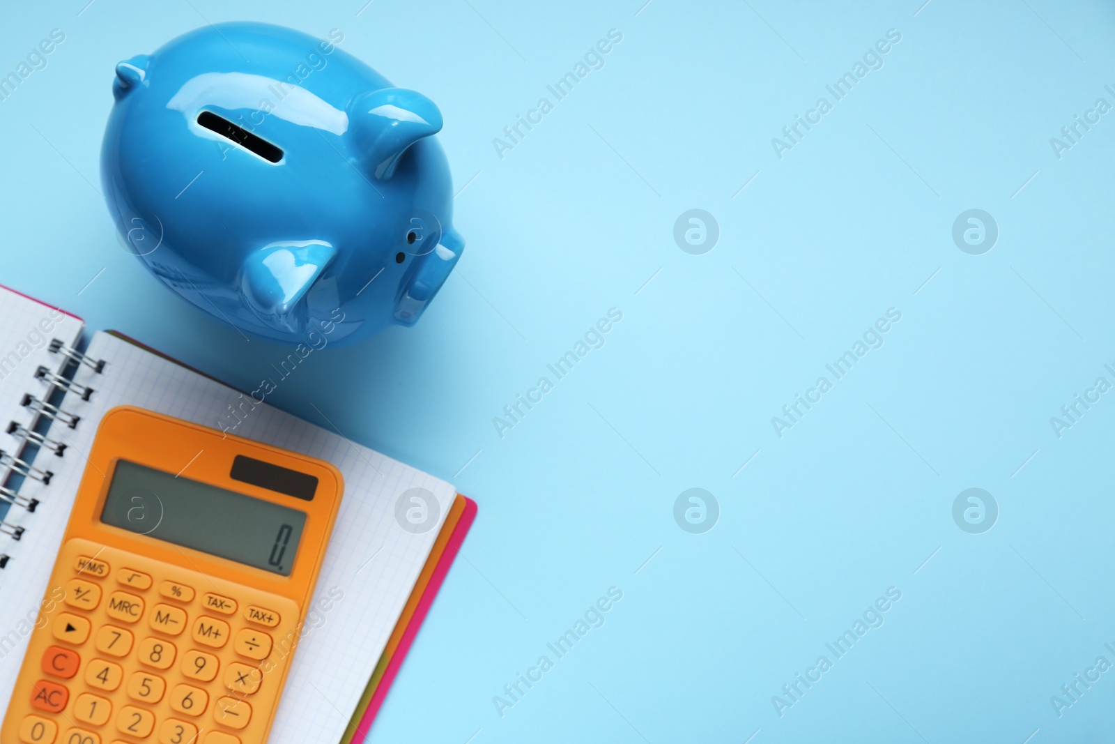 Photo of Piggy bank, notebook and calculator on light blue background, flat lay. Space for text