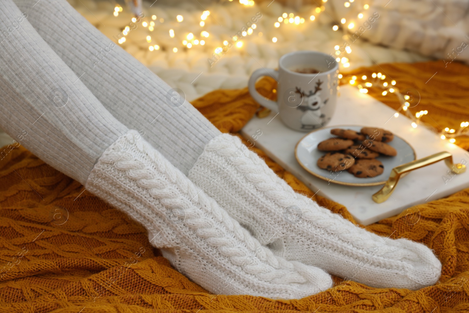 Photo of Woman in warm knitted socks sitting near tray with cup of hot drink and cookies on floor at home, closeup