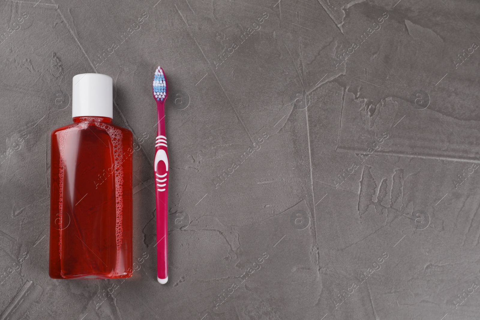 Photo of Fresh mouthwash in bottle and toothbrush on grey textured table, top view. Space for text