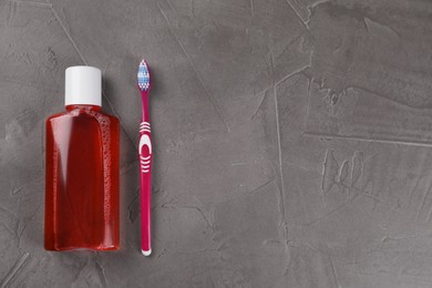 Photo of Fresh mouthwash in bottle and toothbrush on grey textured table, top view. Space for text