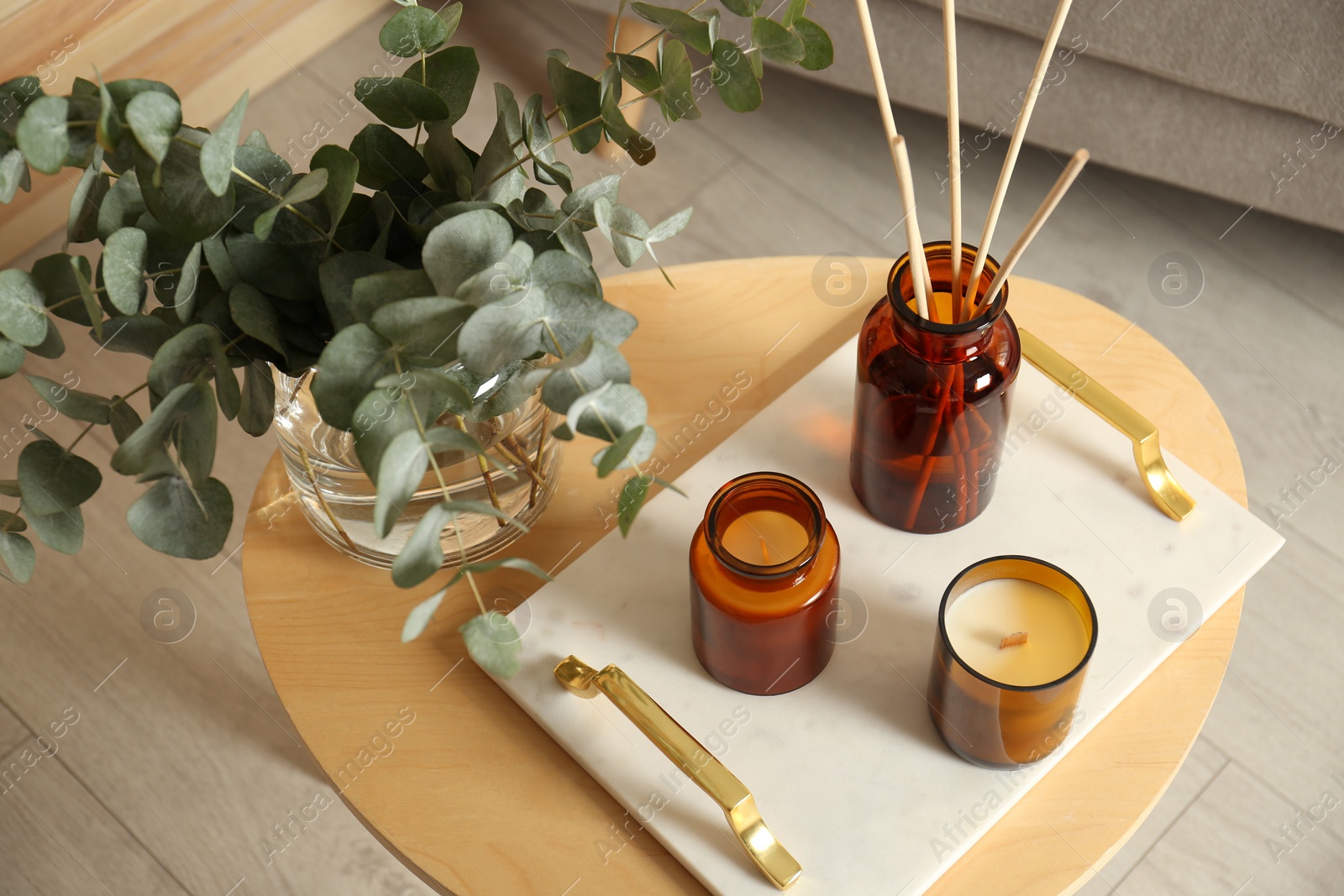 Photo of Eucalyptus branches, aromatic reed air freshener and candles on wooden table in living room. Interior element