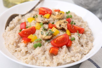 Photo of Delicious barley porridge with vegetables and microgreens in bowl on table, closeup