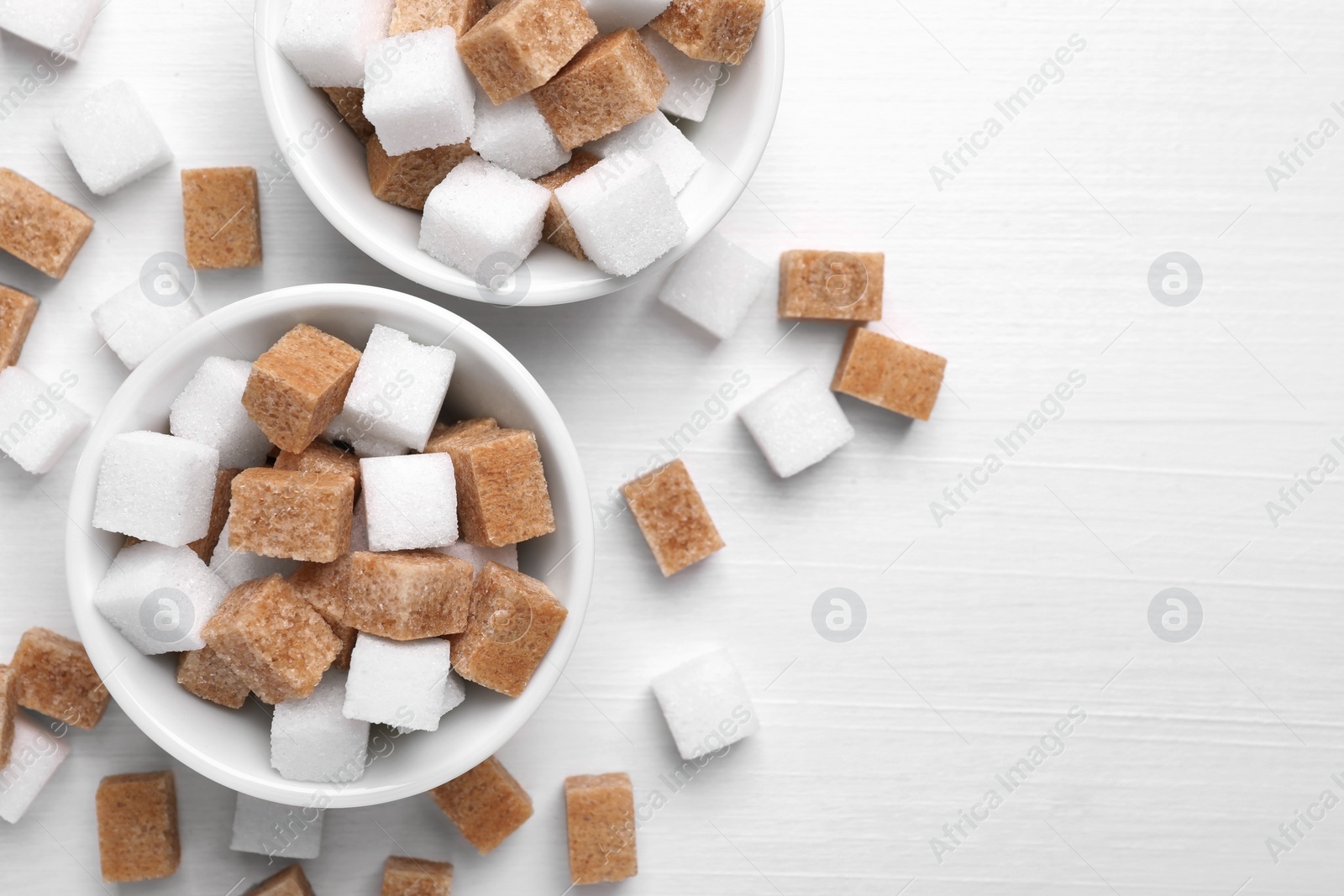 Photo of Different sugar cubes in bowls on white wooden table, flat lay. Space for text