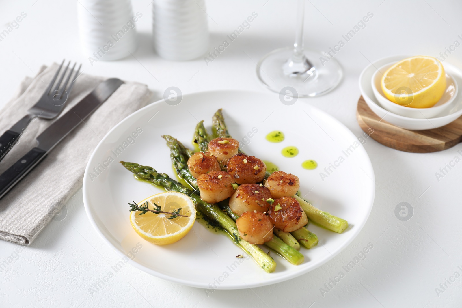 Photo of Delicious fried scallops with asparagus, lemon and thyme served on white table