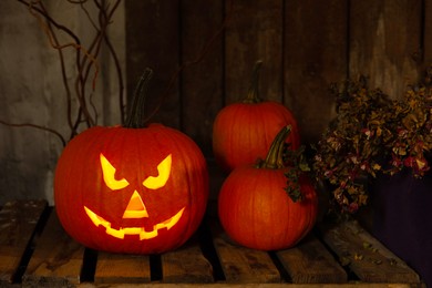 Photo of Scary jack o'lantern pumpkin on wooden bench in darkness. Halloween decor