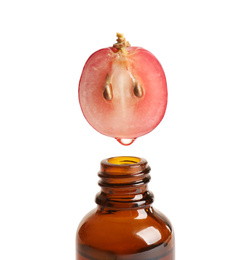 Photo of Natural grape seed essential oil dripping from berry into bottle on white background. Organic cosmetics
