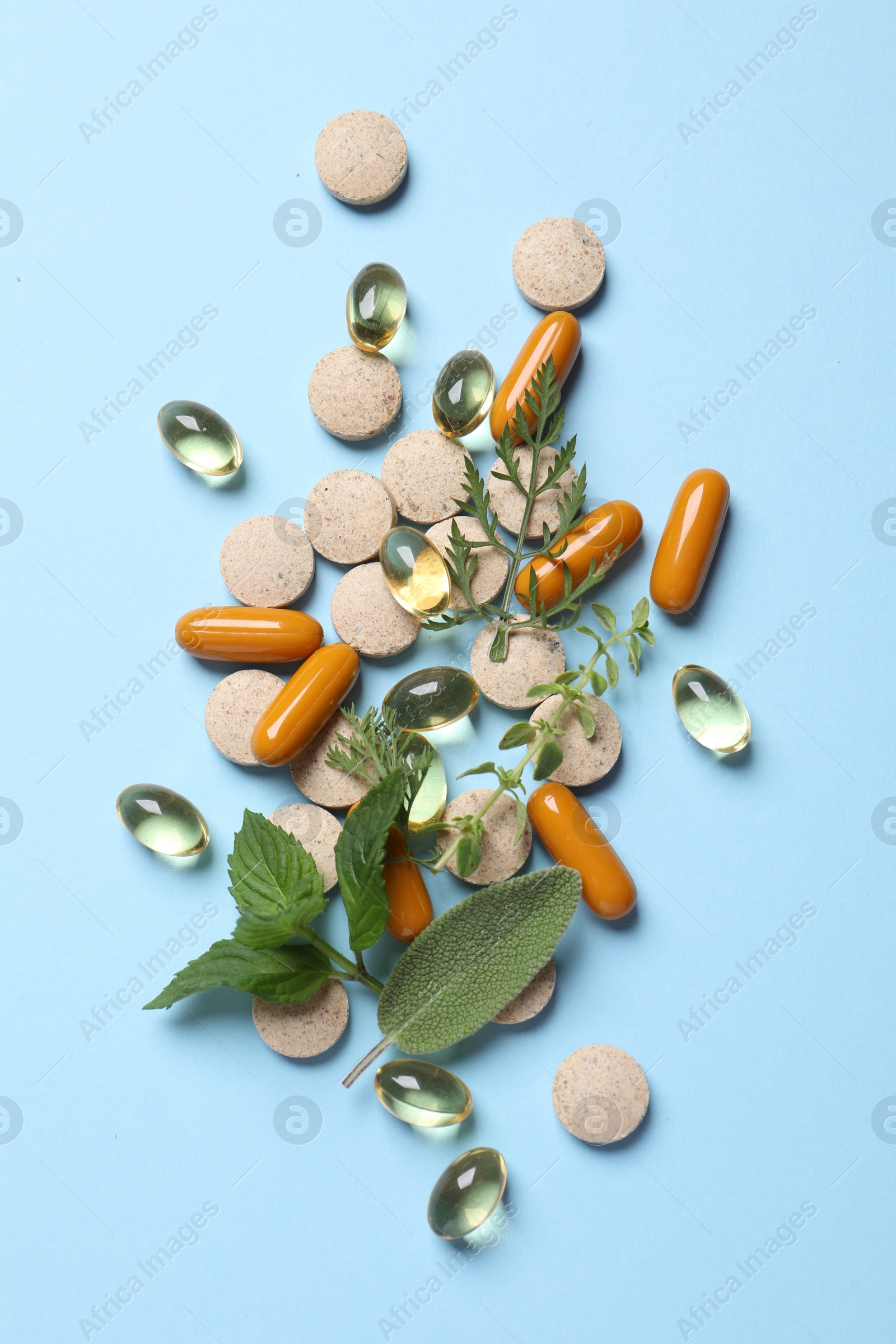 Photo of Different pills and herbs on light blue background, flat lay. Dietary supplements