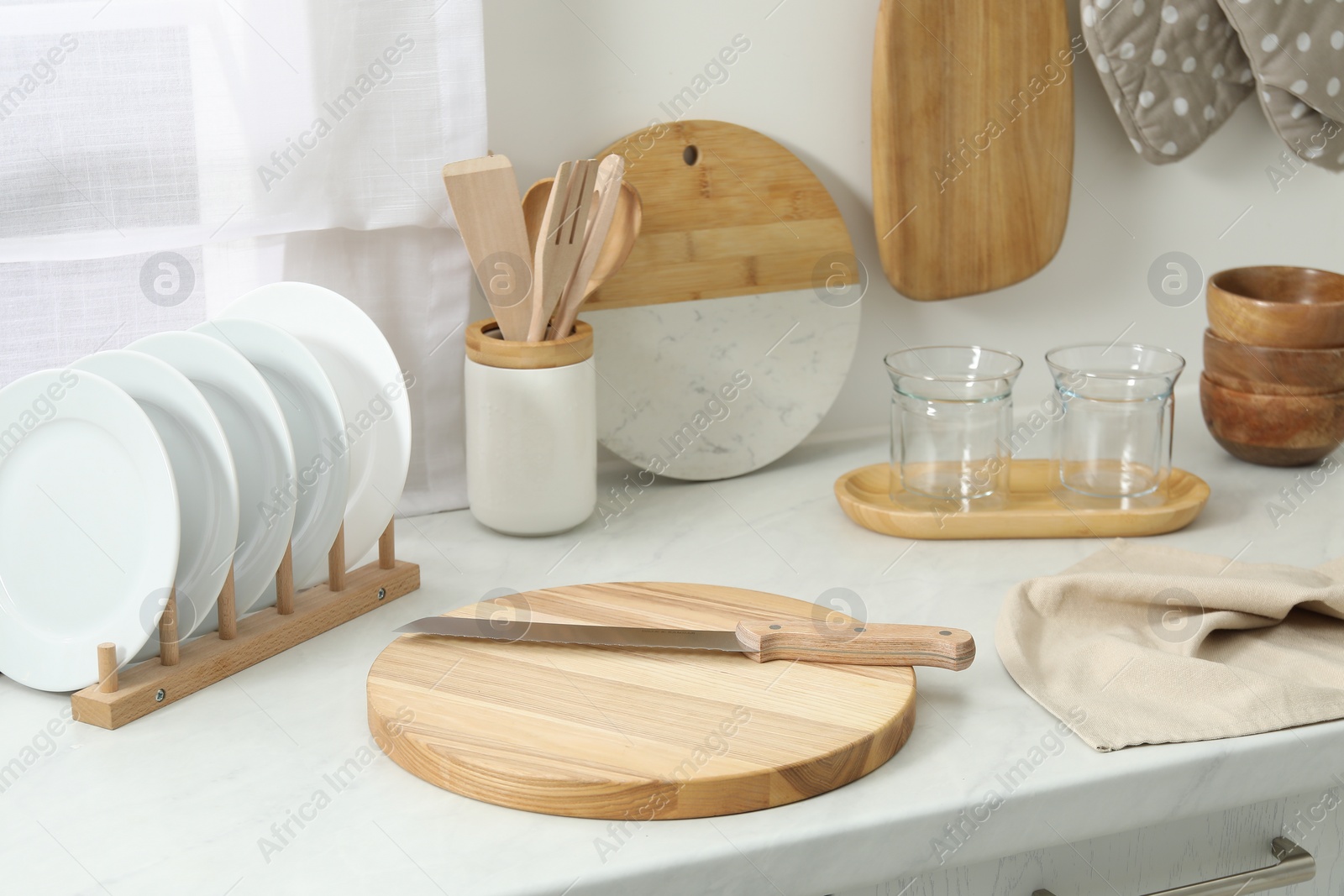 Photo of Wooden cutting boards, other cooking utensils and dishware on white countertop in kitchen