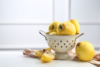 Photo of Tasty ripe quinces and metal colander on white wooden table, space for text