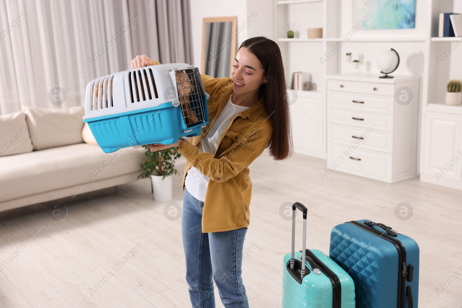 Photo of Travelling with pet. Smiling woman looking at carrier with her dog indoors