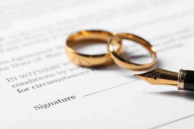 Marriage contract, gold rings and pen on table, closeup