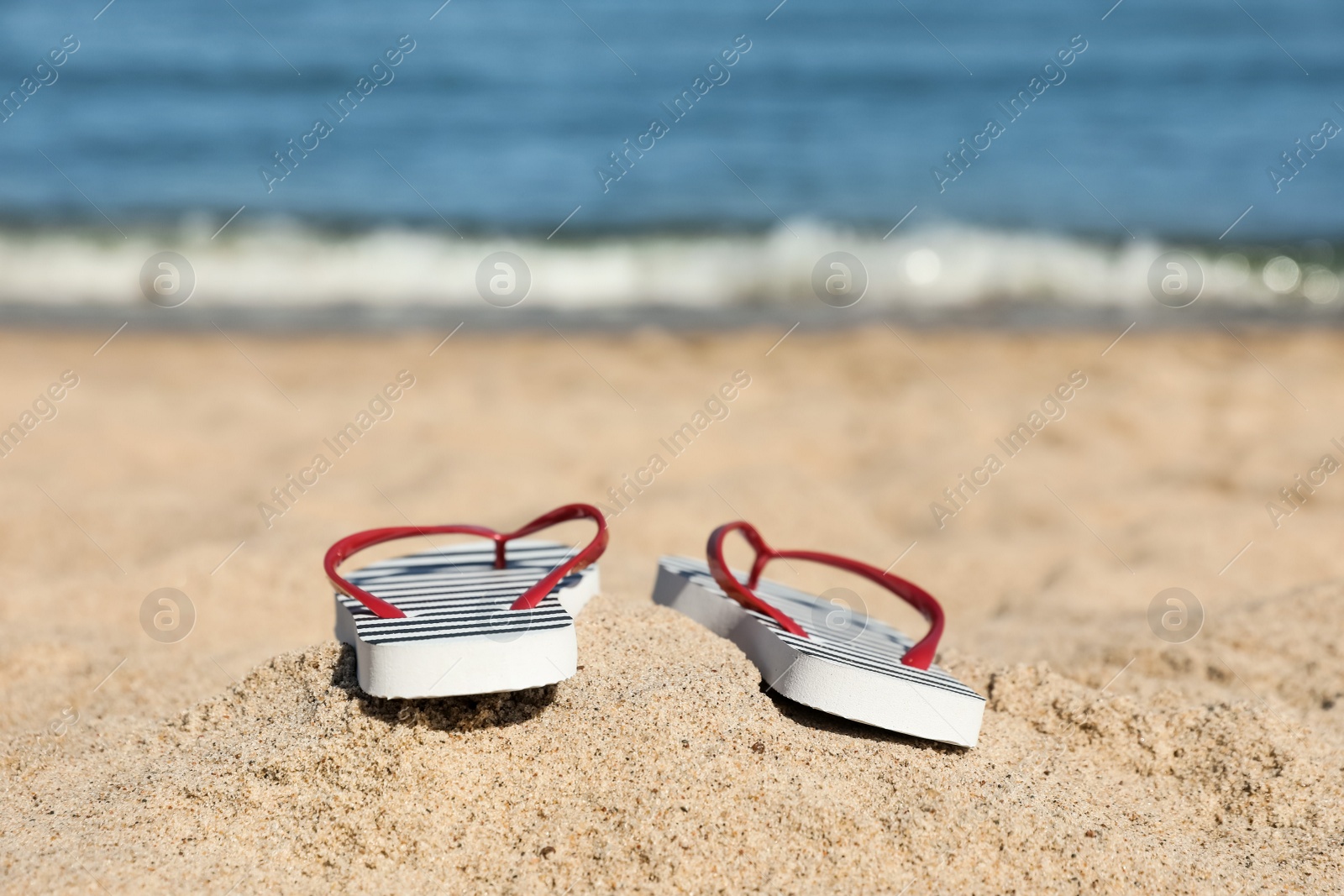 Photo of Striped flip flops on sandy beach near sea