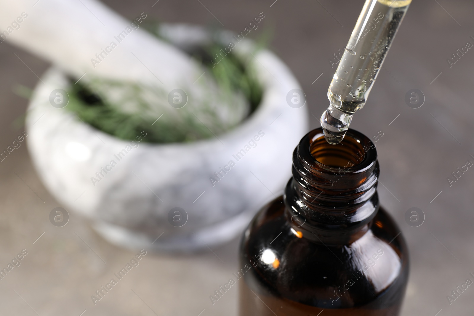 Photo of Dripping dill essential oil from pipette into bottle on blurred background, closeup. Space for text