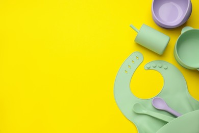 Flat lay composition with baby feeding accessories and bib on yellow background, space for text