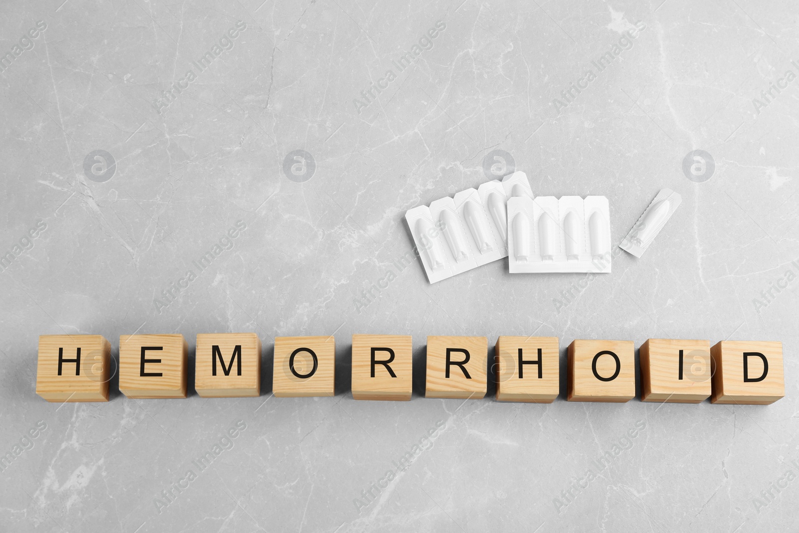 Photo of Wooden cubes with word HEMORRHOID and suppositories on grey marble table, flat lay