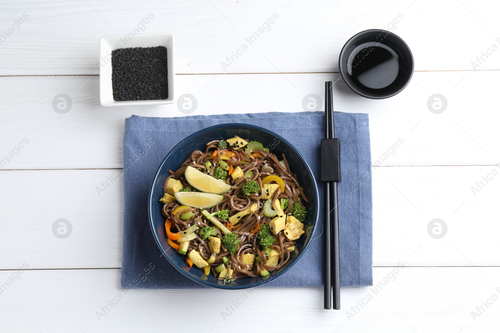 Photo of Stir-fry. Delicious cooked noodles with chicken and vegetables in bowl served on white wooden table, flat lay