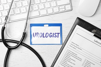 Photo of Badge with inscription UROLOGIST, clipboard, keyboard and stethoscope on table, top view