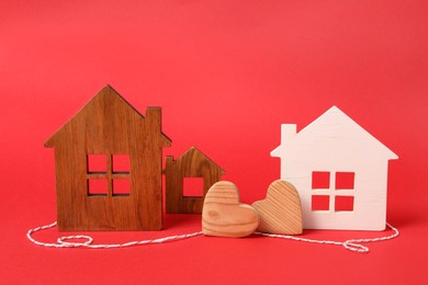 Photo of Wooden hearts and decorative cord between house models on red background symbolizing connection in long-distance relationship