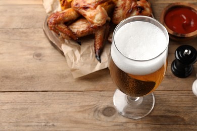 Glass of beer, delicious baked chicken wings and sauce on wooden table, space for text