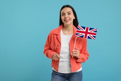Happy young woman with flag of United Kingdom on light blue background