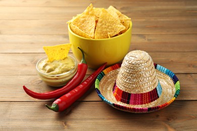 Photo of Mexican sombrero hat, chili peppers, nachos chips and guacamole on wooden table