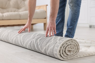 Man unrolling carpet with beautiful pattern on floor in room, closeup