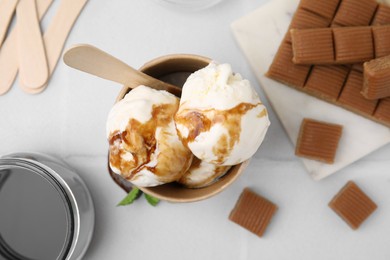 Photo of Scoops of ice cream with caramel sauce and candies on white table, flat lay