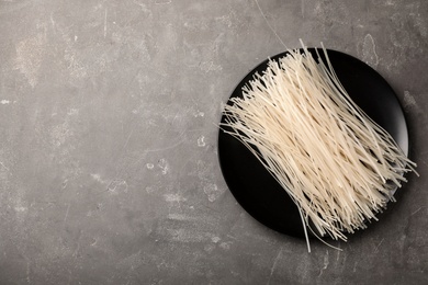 Photo of Plate with raw rice noodles on grey background, top view. Space for text