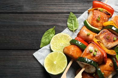Photo of Delicious chicken shish kebabs with vegetables and lime on black wooden table, top view. Space for text