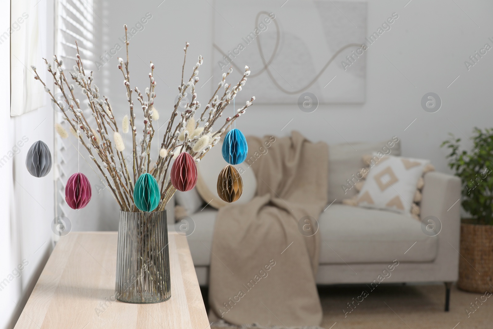 Photo of Beautiful pussy willow branches with paper eggs in vase on wooden table at home, space for text. Easter decor