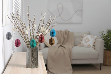 Beautiful pussy willow branches with paper eggs in vase on wooden table at home, space for text. Easter decor