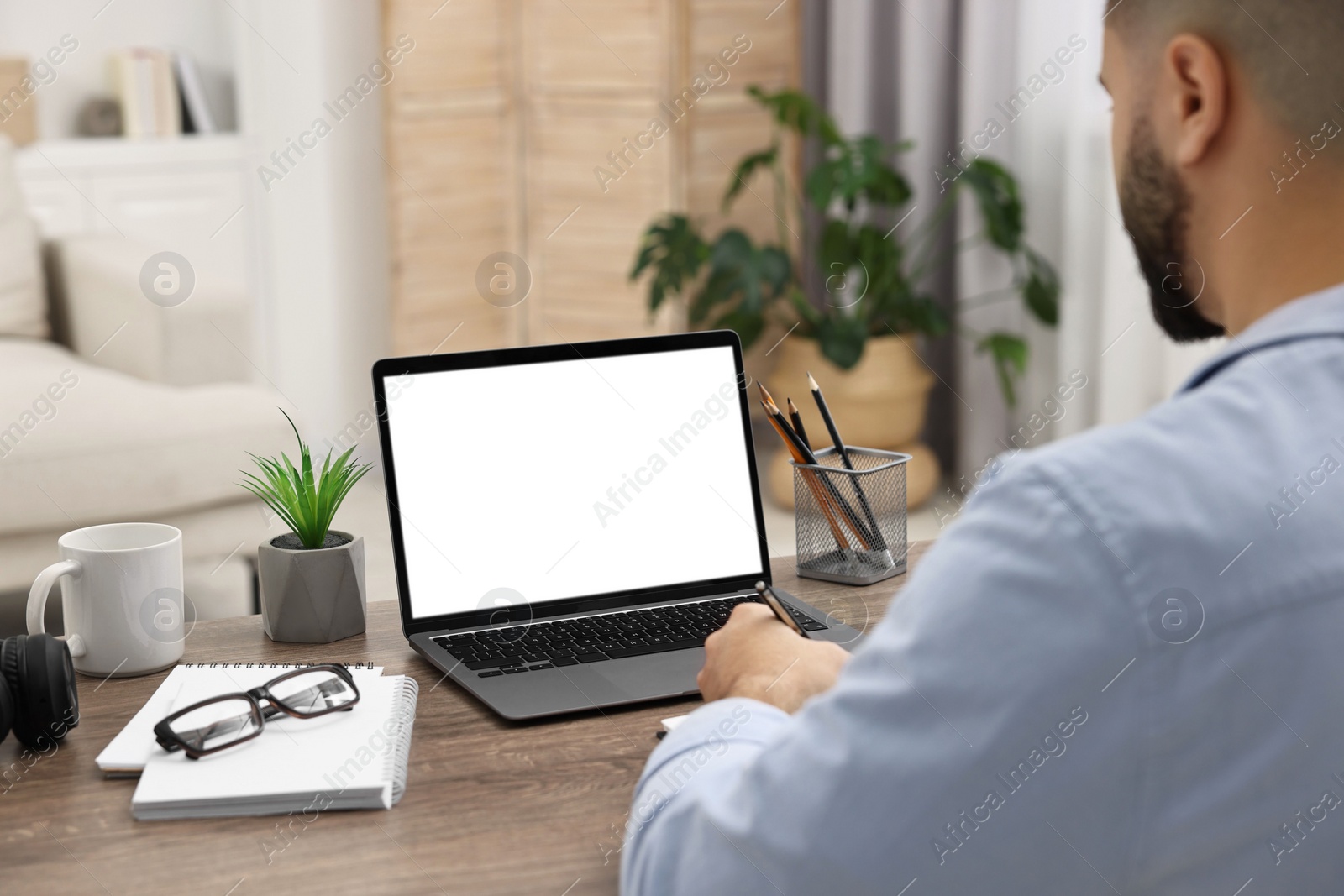 Photo of E-learning. Young man using laptop at wooden table indoors, closeup