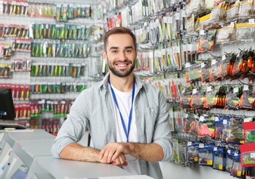 Photo of Salesman standing near showcase with fishing equipment in sports shop