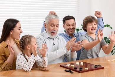 Photo of Emotional family playing checkers at wooden table in room