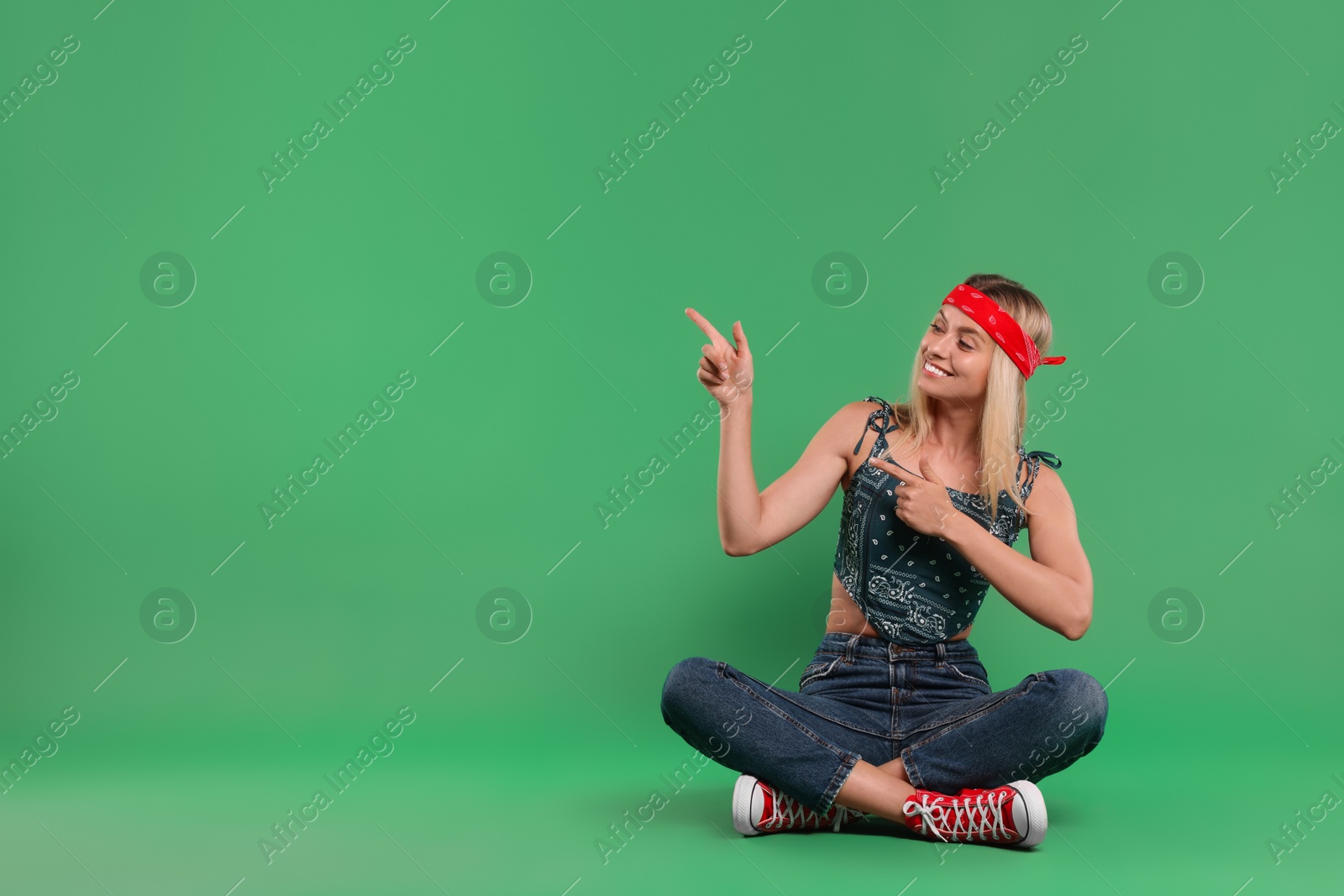 Photo of Portrait of happy hippie woman pointing at something on green background. Space for text