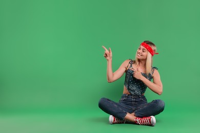 Portrait of happy hippie woman pointing at something on green background. Space for text